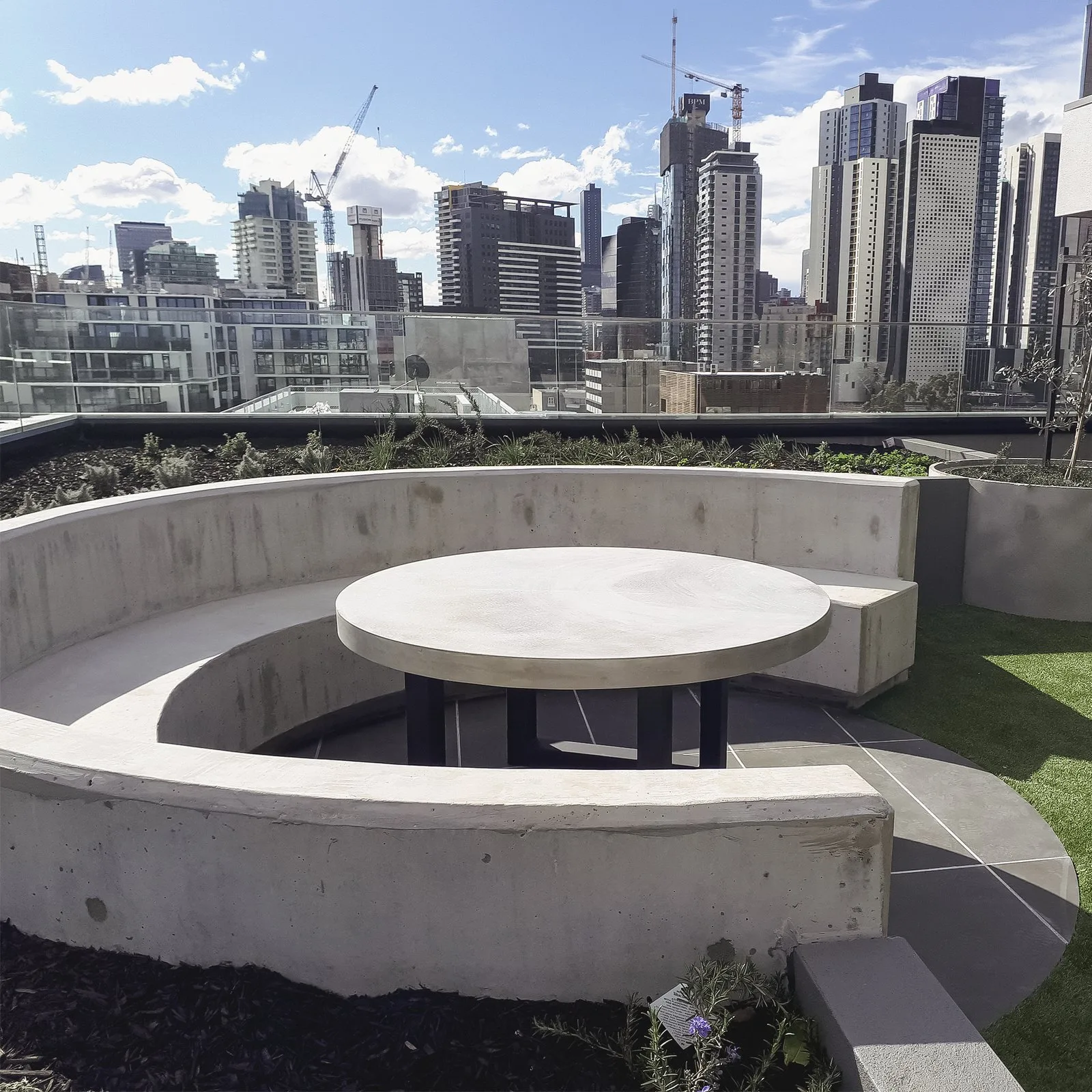 Custom concrete circular bench seat and round table on a Melbourne rooftop terrace, a public-space commercial commission overlooking the CBD skyline